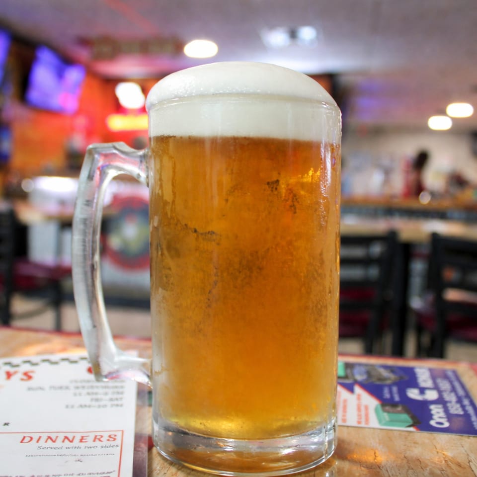 A frosty mug of beer with a thick head of foam sits on a table with menus.