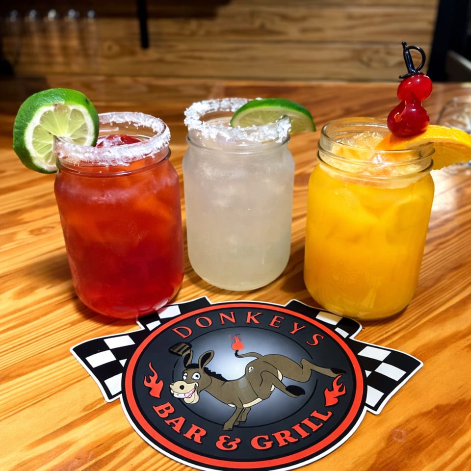 Three colorful drinks in mason jars with fruit garnishes and the Donkeys Bar & Grill logo.