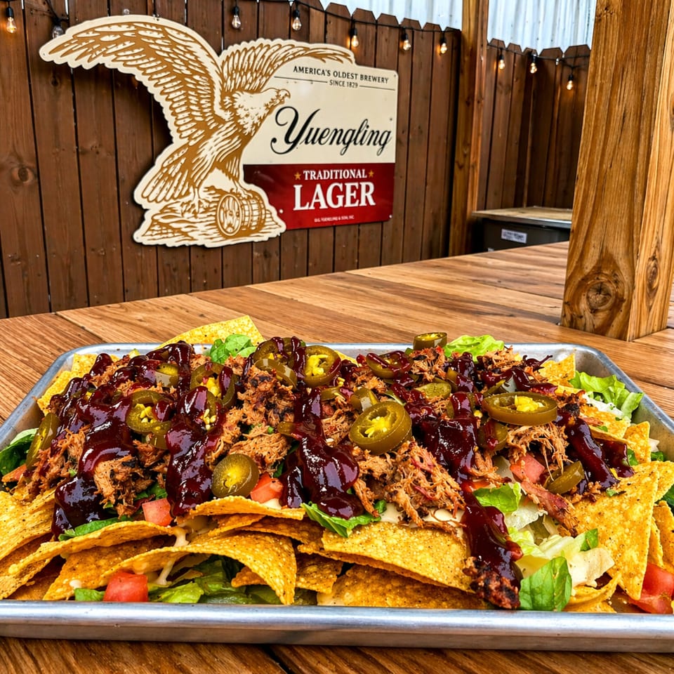 A large tray of nachos with pulled pork, jalapeños, and barbecue sauce on a wooden table.