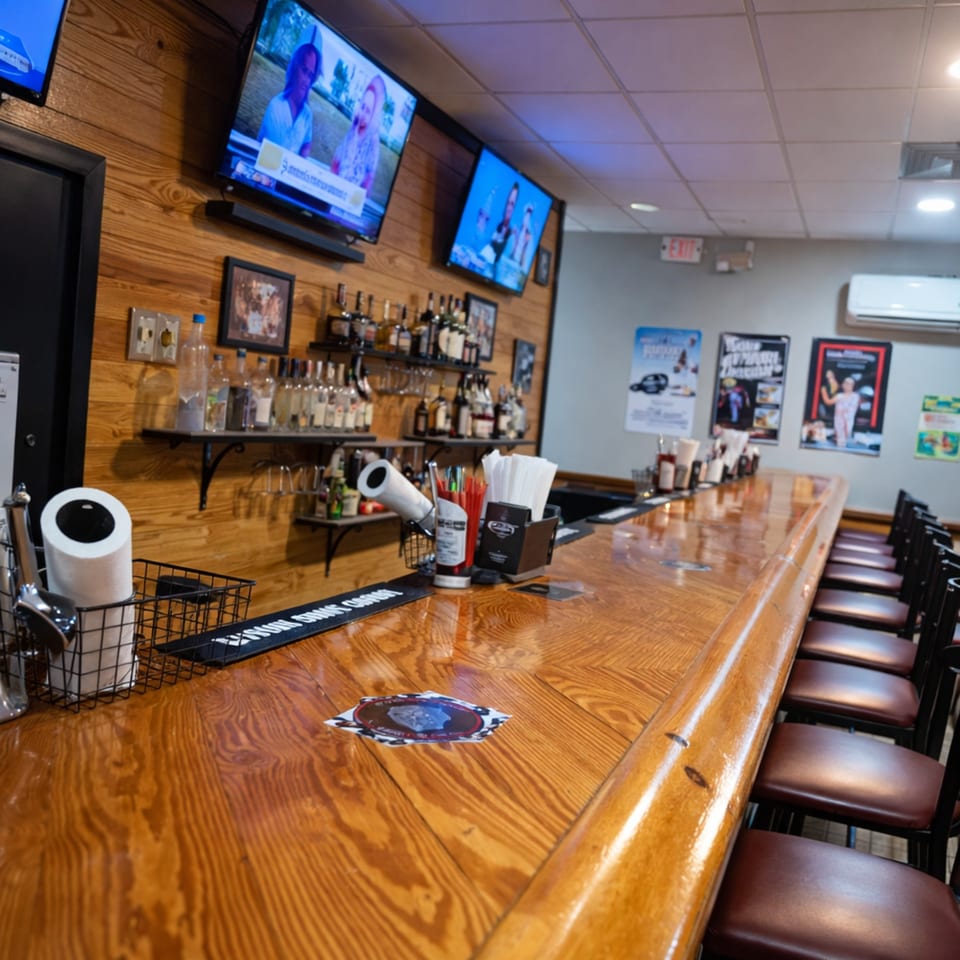 A long, polished wooden bar with stools, liquor bottles, and TVs on a wood-paneled wall.